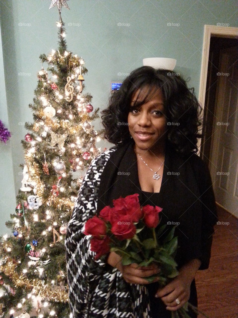 African woman standing in front of illuminated christmas tree with rose bouquet in hand