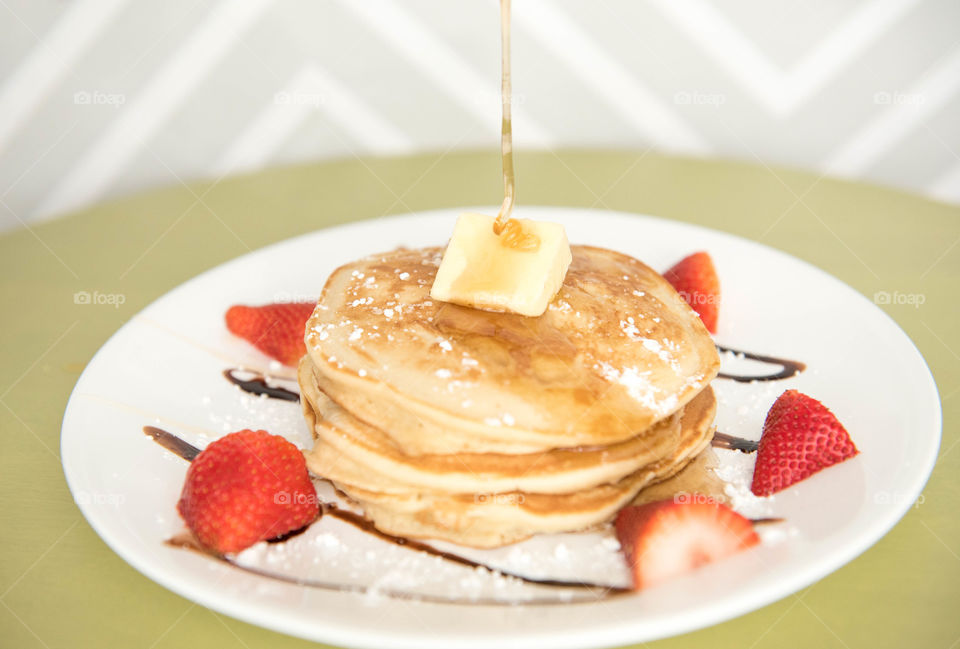 Motion of syrup being drizzled on top of a stack of pancakes with strawberries