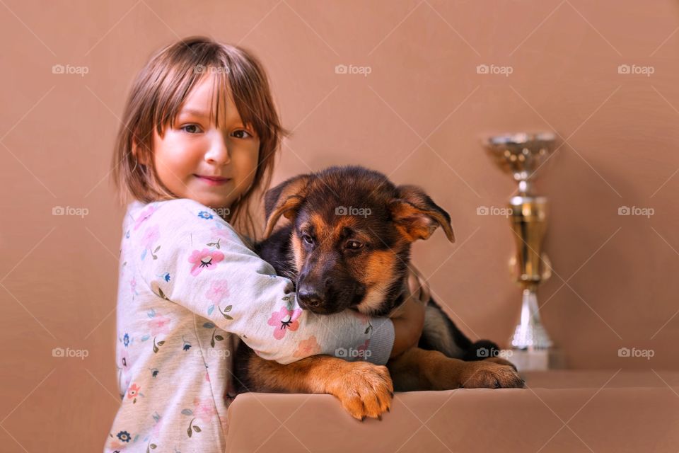 Little girl with German shepherd puppy on light brown background 