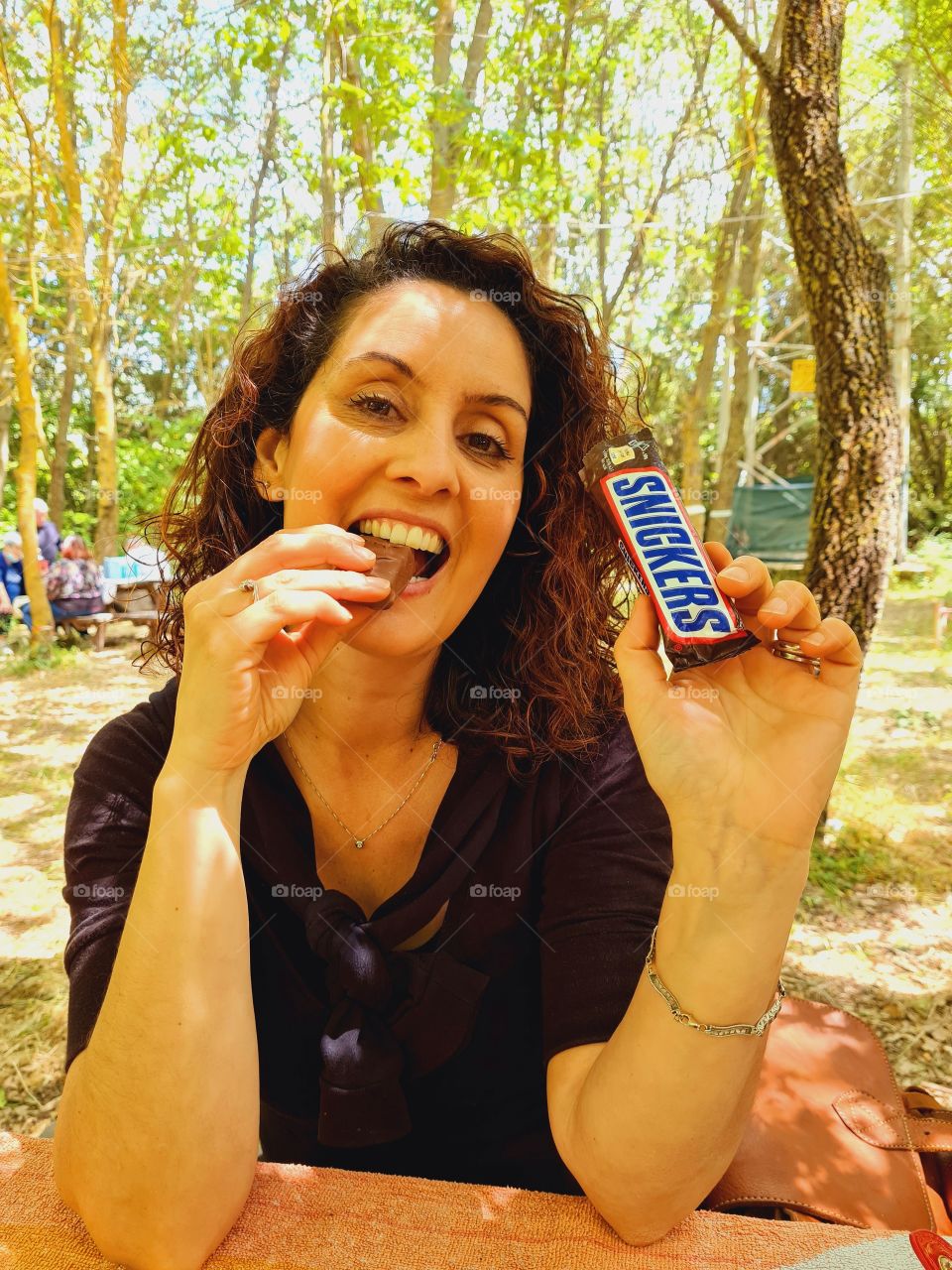 Smiling Woman satisfied eats her Snickers at the park
