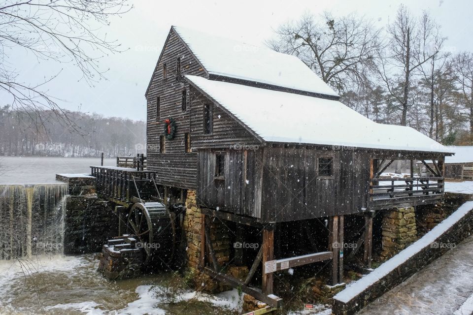 A festive view of the old rustic water mill as snow falls during the Christmas season at Historic Yates Mill County Park in Raleigh North Carolina. 