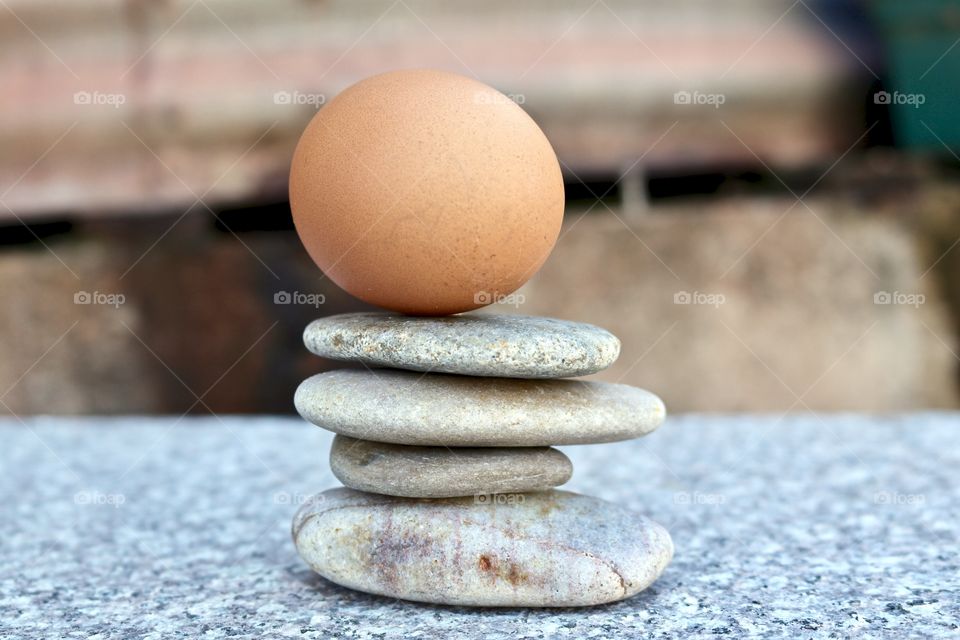 Brown egg balancing atop smooth stone rock pile stack on marble surface, concept life, business, ideas, creativity endurance or stability
