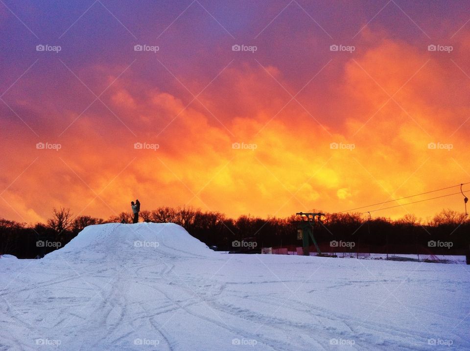 Cold and hot. Fiery sunset above snow ski park. Father and daughter standing on the big snow tramp