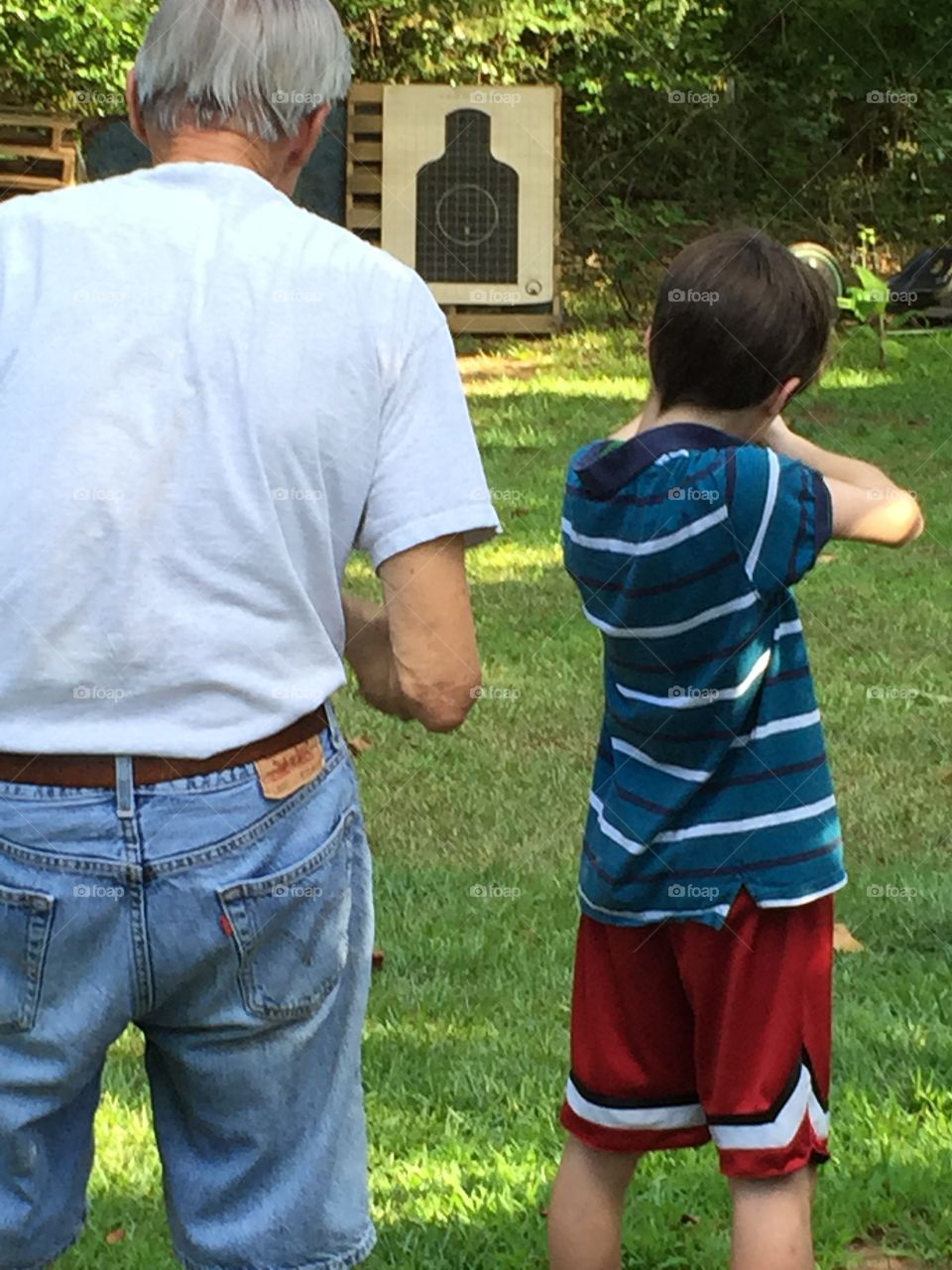 Grandpa and his young grandson, practicing shooting at a paper target.