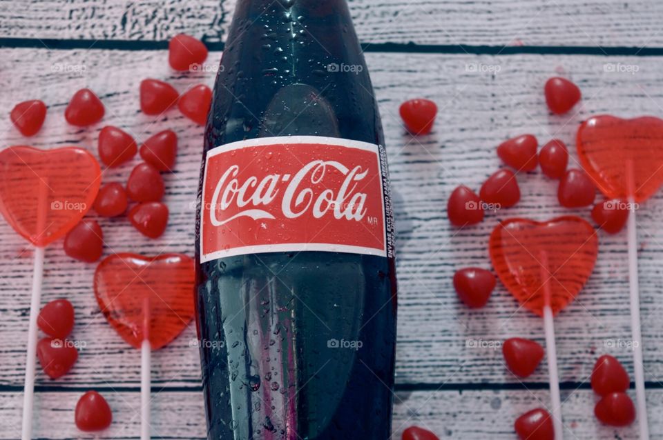 A glass bottle of Coca-Cola with candy hearts and a white rustic background