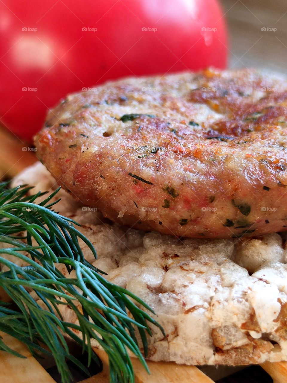 Food.  On the cereal bread there is a meat cutlet and a sprig of dill.  There is a red tomato in the background