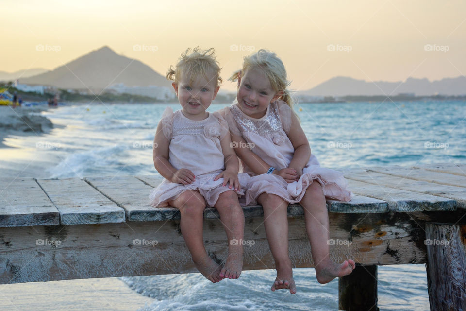 Two little girl sitting on pier at beach