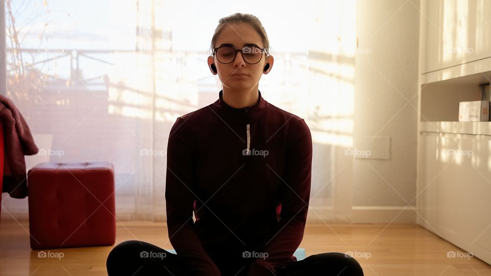 A teenage girl practices meditation while listening to music on wireless headphones 