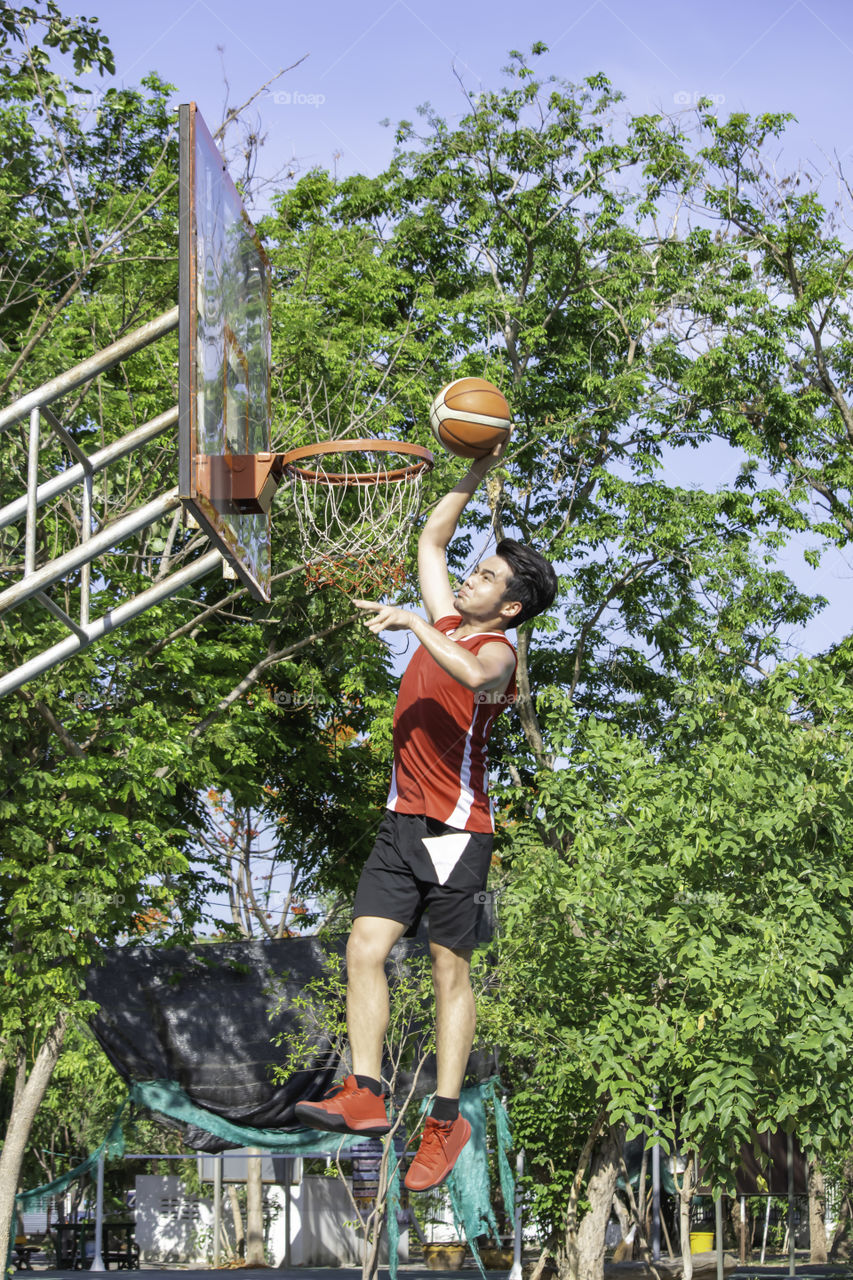 Man holding a basketball jumping Throw a basketball hoop Background blur  tree in park.