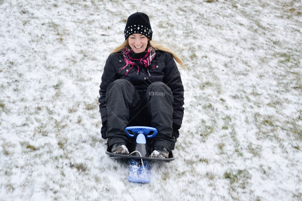 A woman of 30 years of age go sledding in the snow.