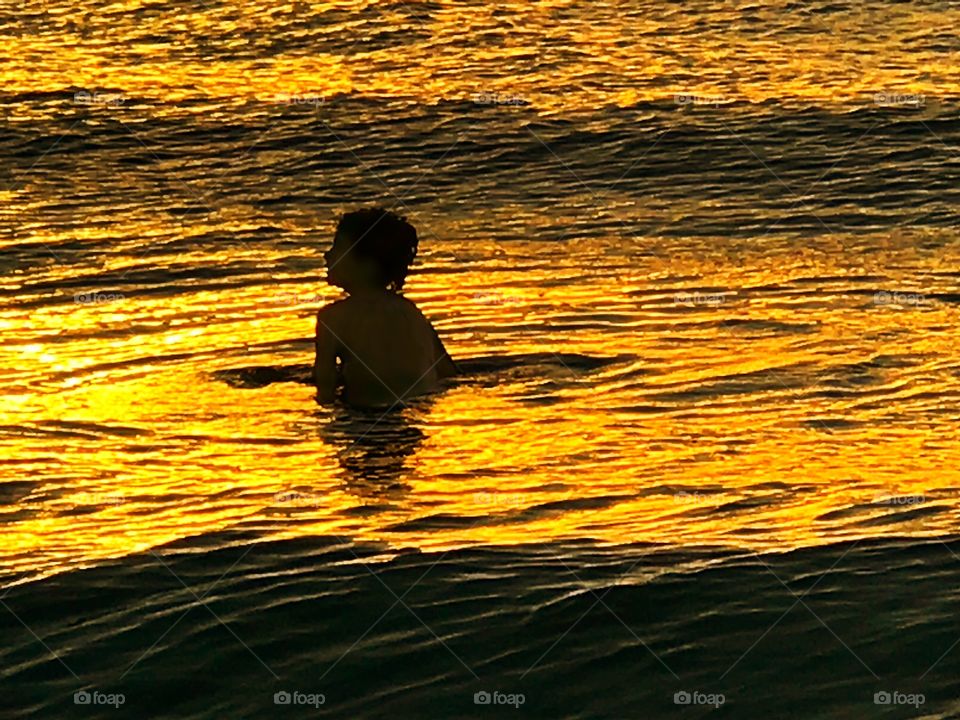 Boy in the golden waves of an ocean sunset.