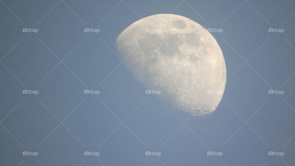 Close-up of Moon with craters during the day against blue sky