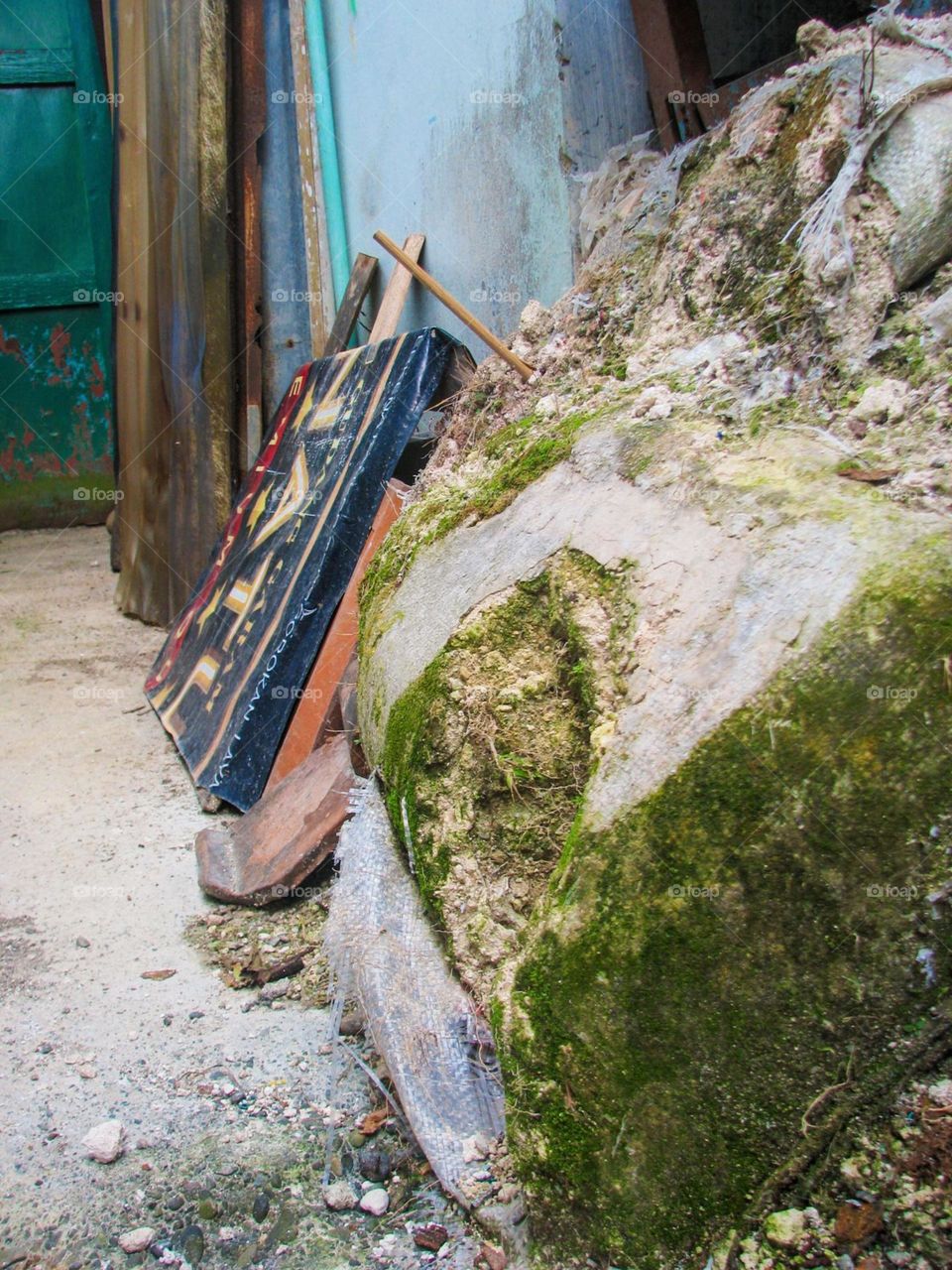 Banyumas, Central Java, Indonesia - January 20, 2024: Portrait of a large rock covered in moss, with planks and wooden sticks leaning against it, placed outside an old building