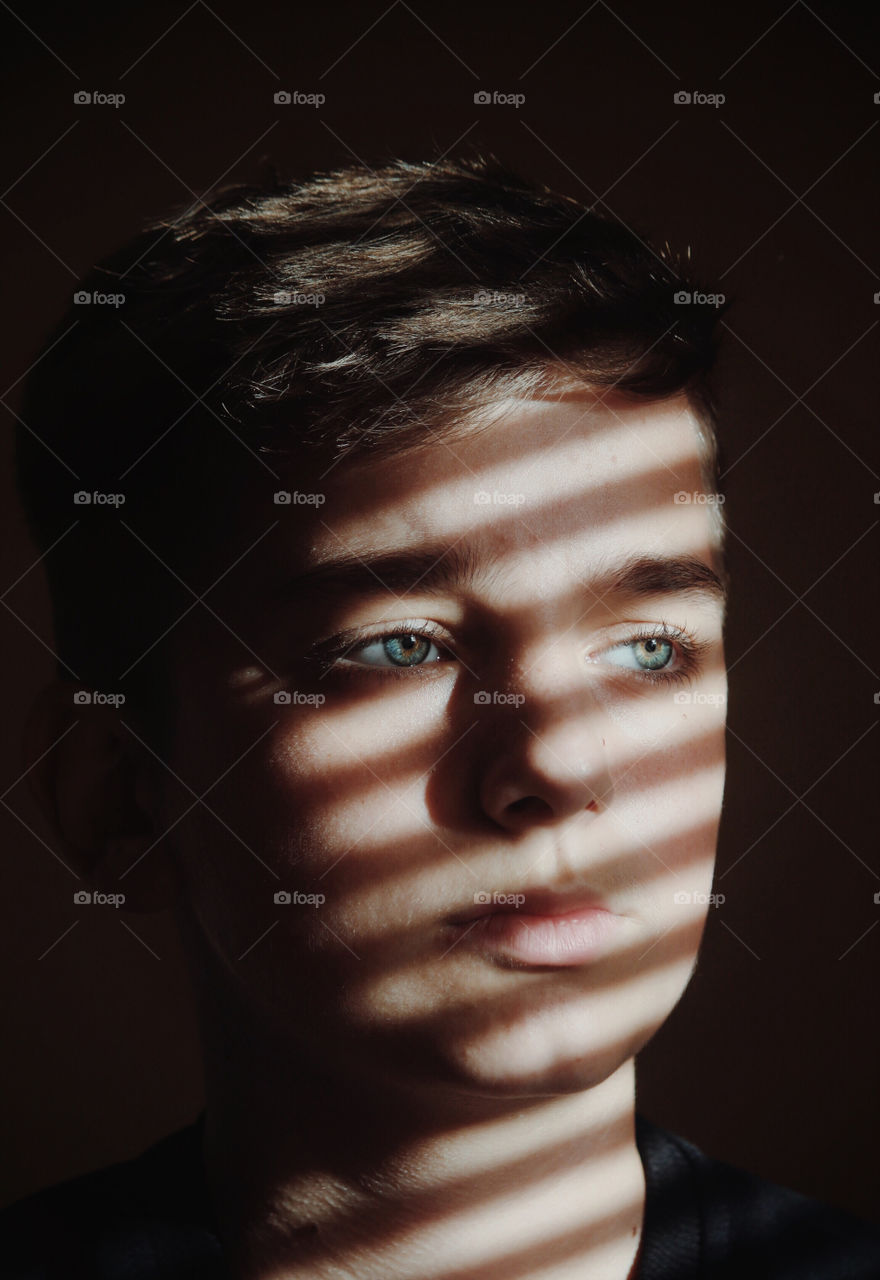 Close-up of thoughtful boy looking away against wall with sunlight falling on his face. 