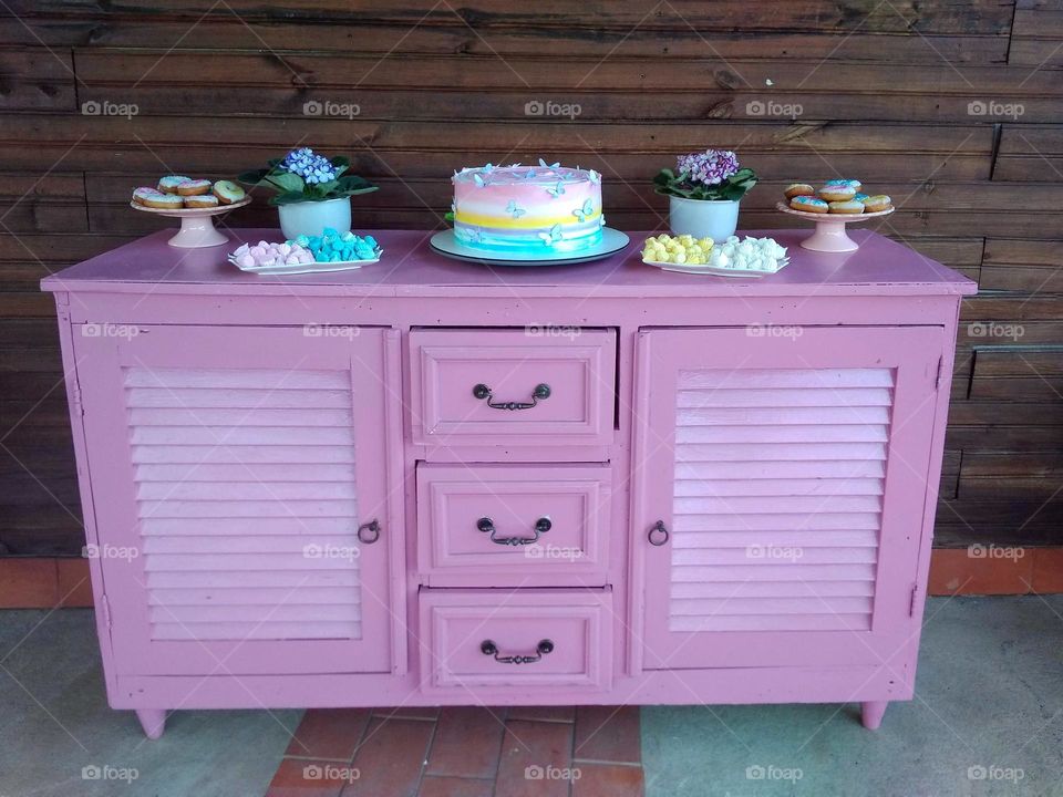 A drawer cabinet as a birthday table, with cake, flower vases and sweets.Wood background