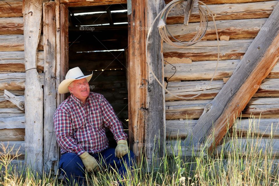 Senior man sitting near barn wearing hat