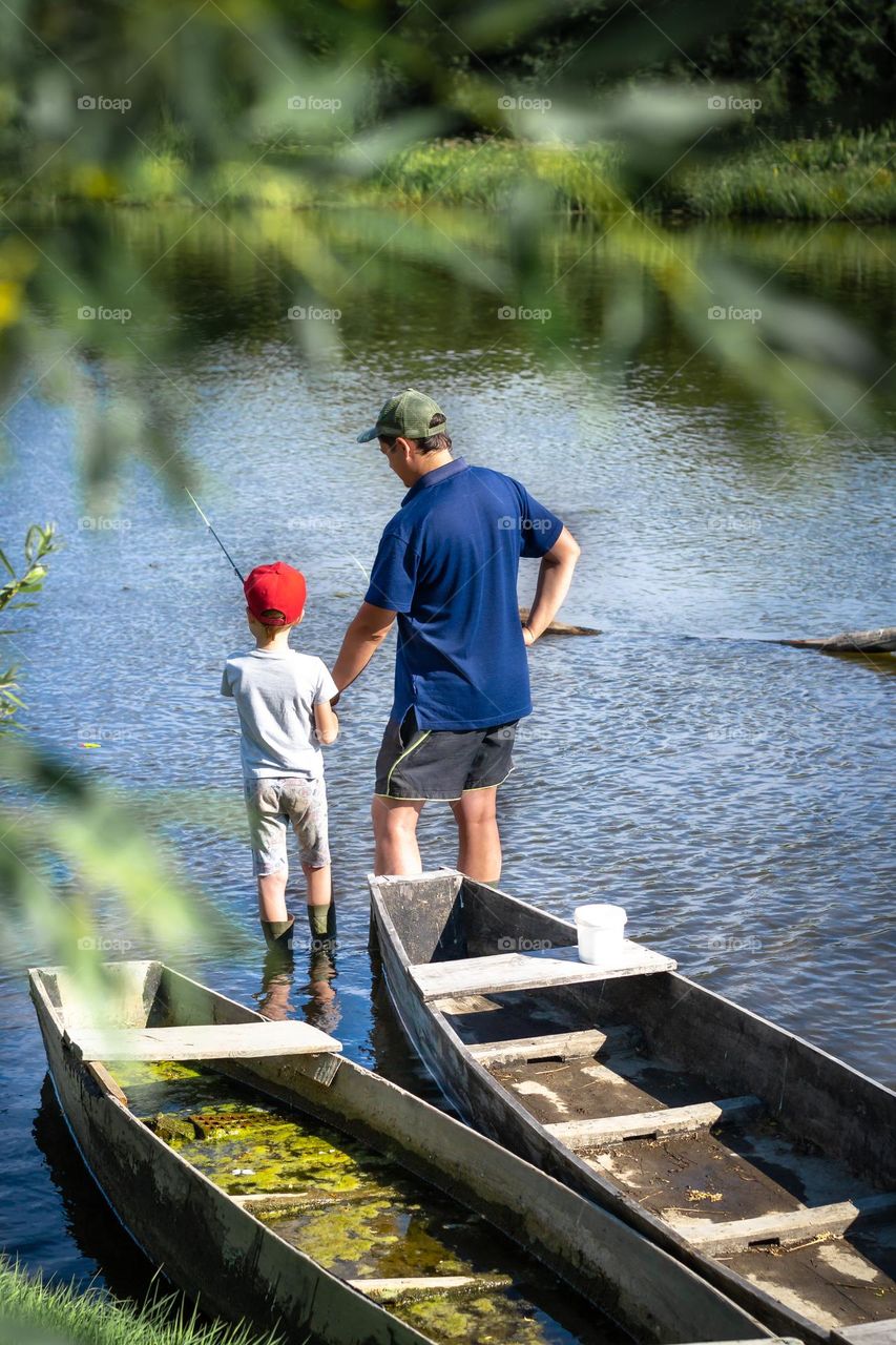 Father and son are fishing on the river in the summer in the village. Family fun, dad time