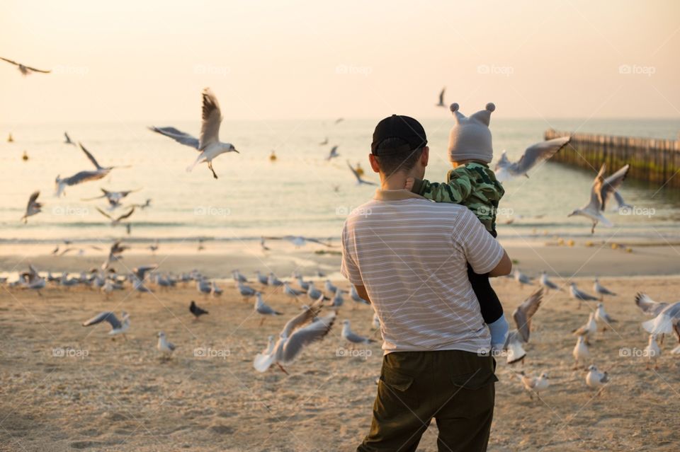 Father with small son feeds seagulls at the sunset beach