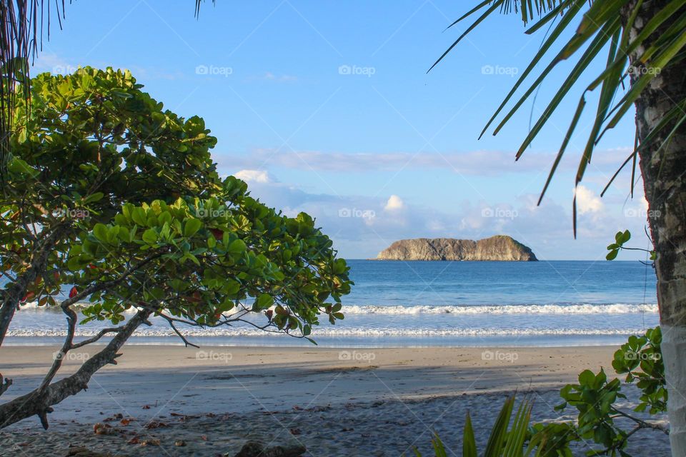 View through the branches to the sandy beach and island in the distance.  Summer landscape in Costa rica