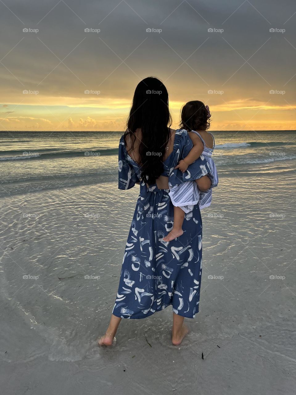 The back of mother and daughter watching the sunset at the beach together.