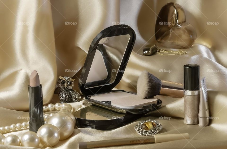 Assorted cosmetics in neutral tones, which jewellery and perfume against a silky golden background 