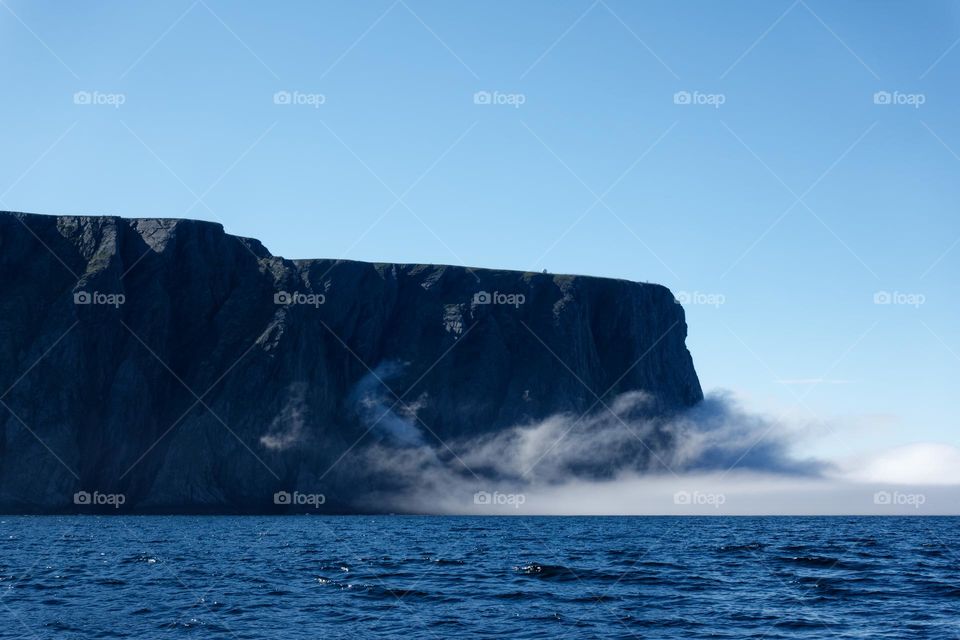 The northernmost tip of Europe, a large rock cliff of North Cape or Nordkapp on summer day with dramatic sea fog rising on Mageroya island in Finnmark in Northern Norway. 