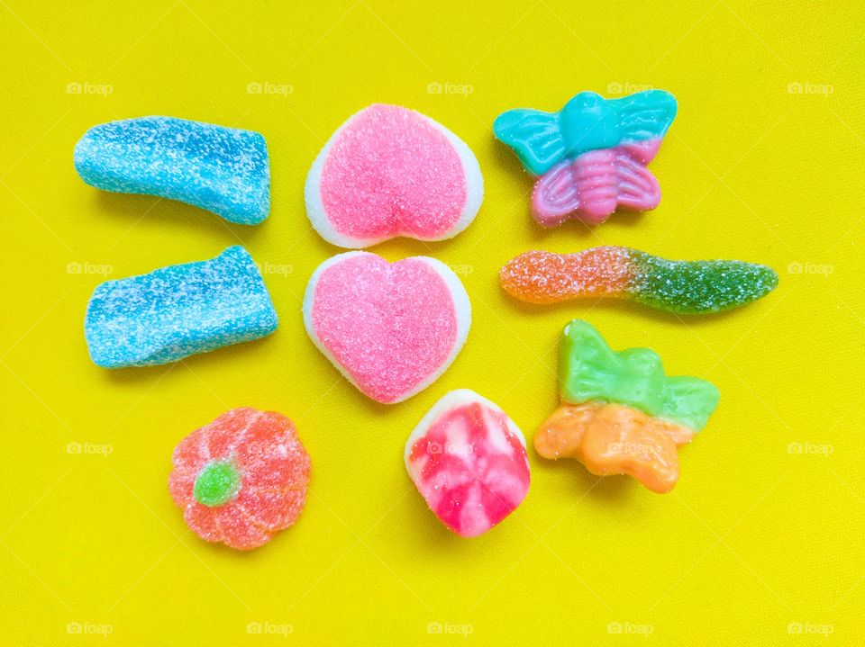mixture of beautiful colorful candy in different shapes on yellow background