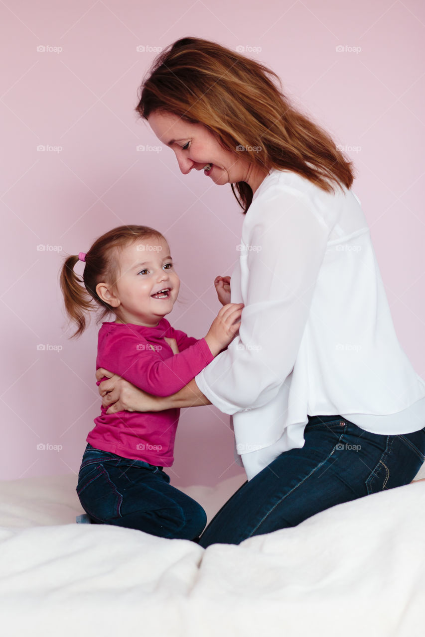 Happy mother and daughter sitting on bed