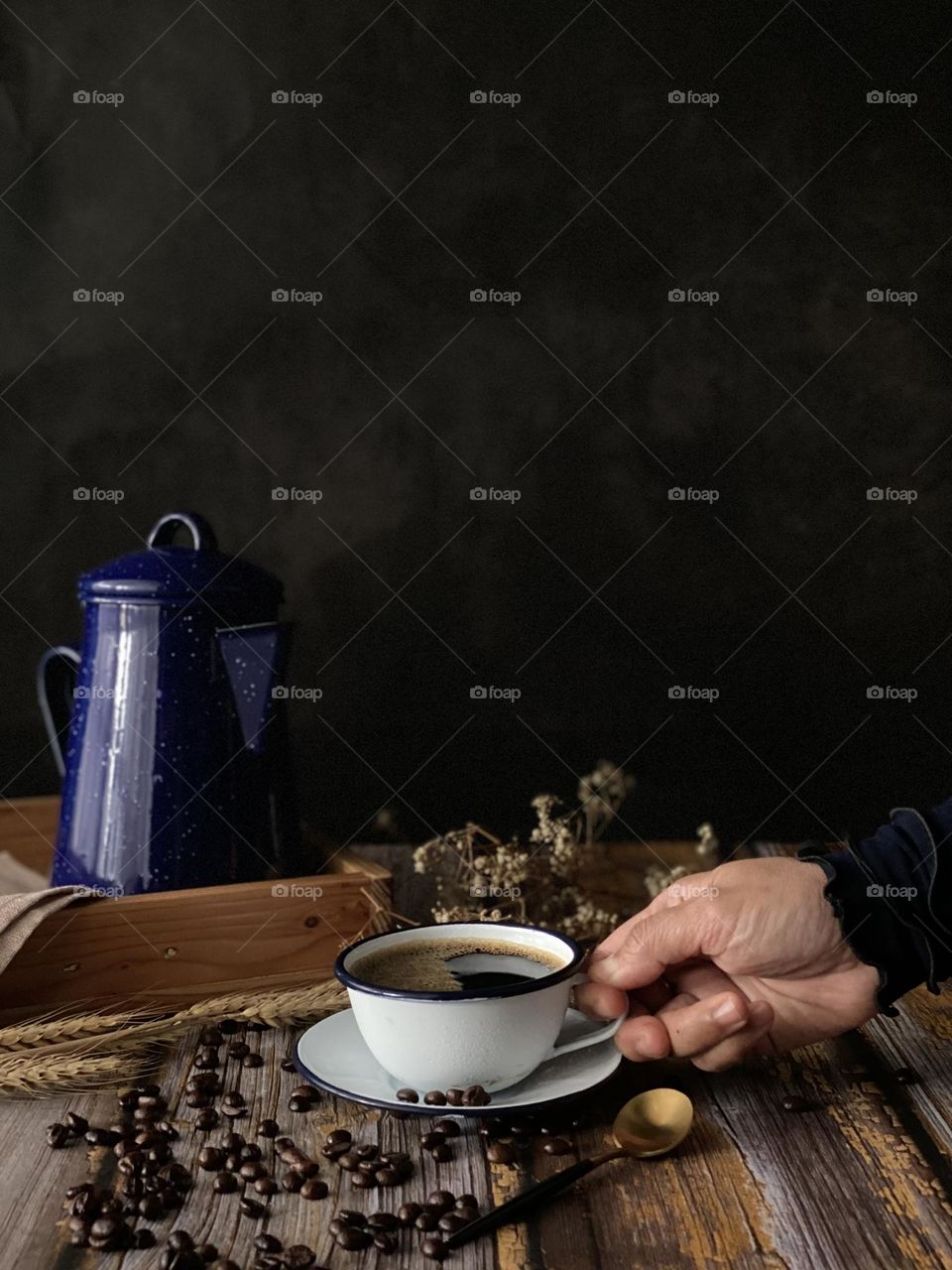 Hands take a cup of black coffee. Background of a teapot and sprinkles coffee beans on the table.