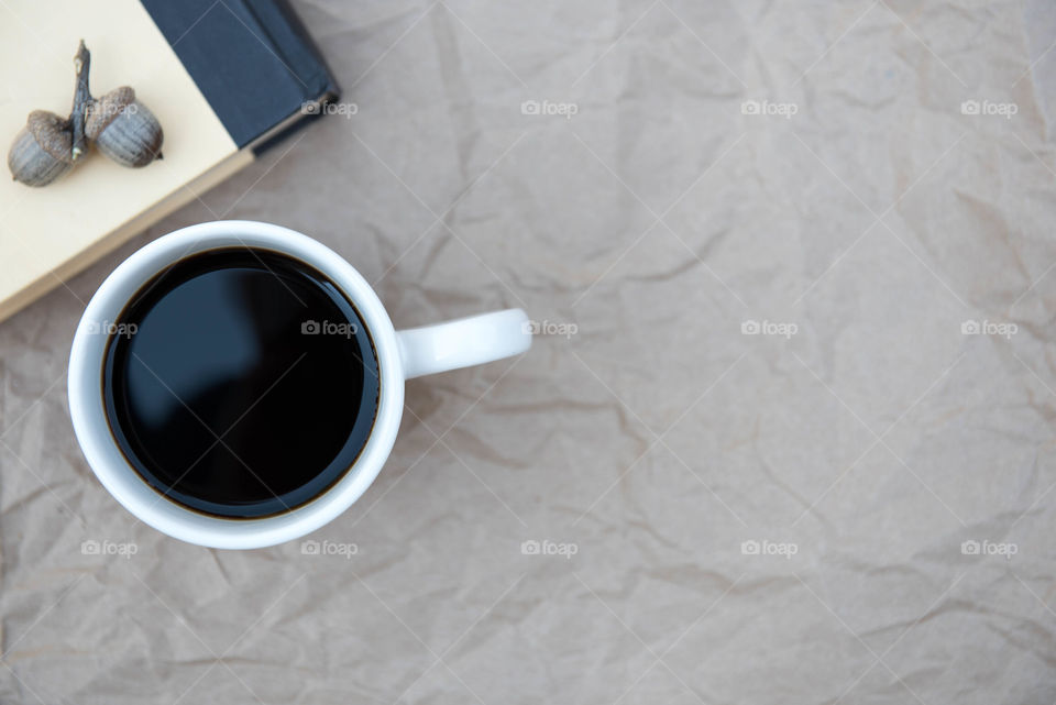 Monochromatic flat lay of a cup of coffee, book and acorns