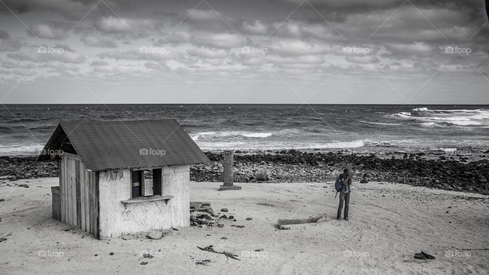 The photograph depicts a hut in the middle of a beach along with a photographer doing his work.