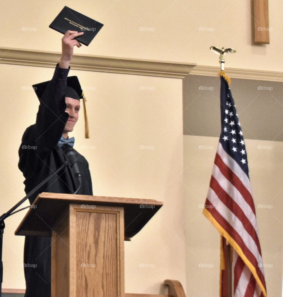 Graduate holding up his diploma, flag in the background 