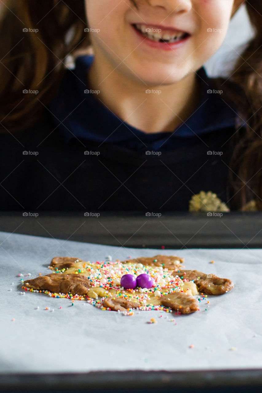 Baking at home - my girl holding up her little 'corona bug' cookie - using fun to create and educate in hard times. Girl smiling and loving her decorated cookie ready to go into the oven.