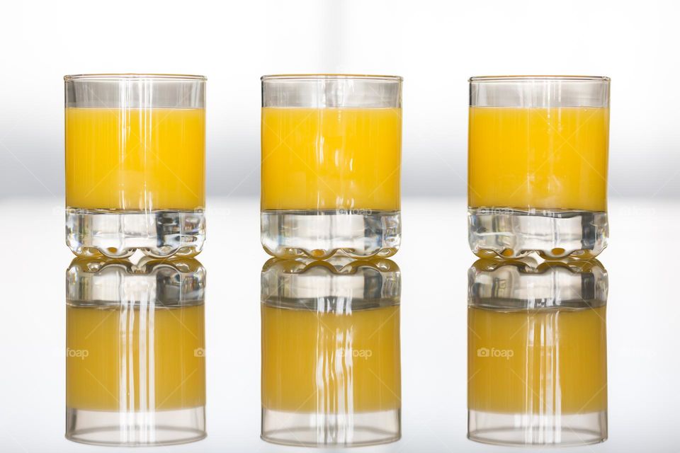 Three glasses filled with cold fresh orange juice, reflection in the countertop 