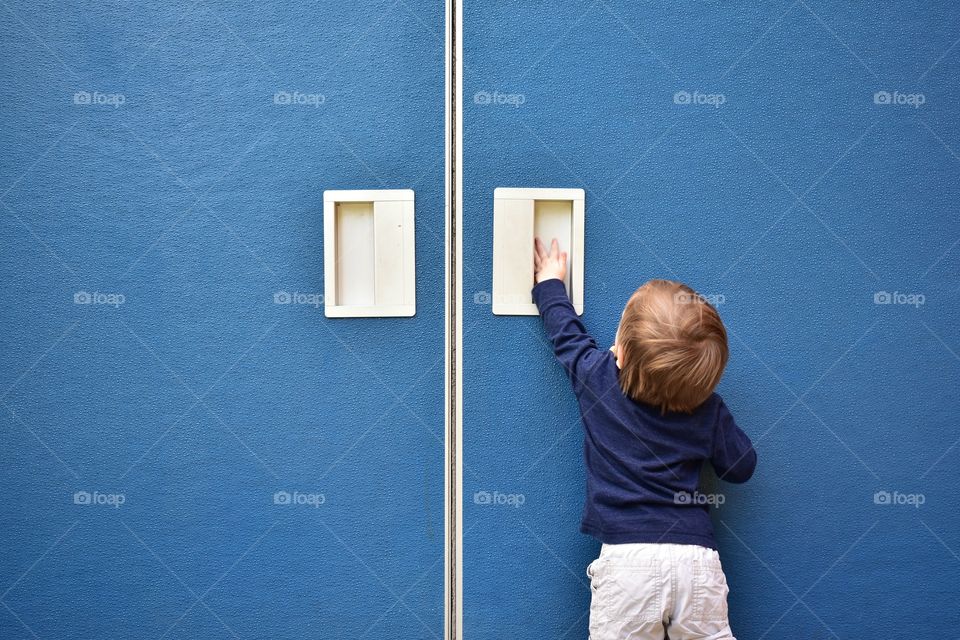Cute toddler boy trying to open blue door 