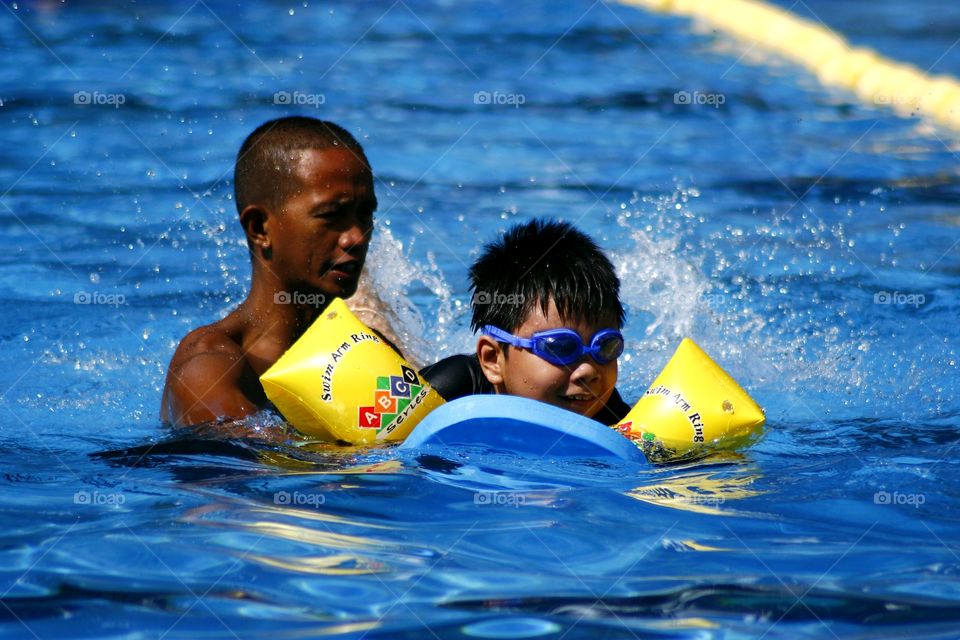 young kid learns how to swim with the help of a swimming coach