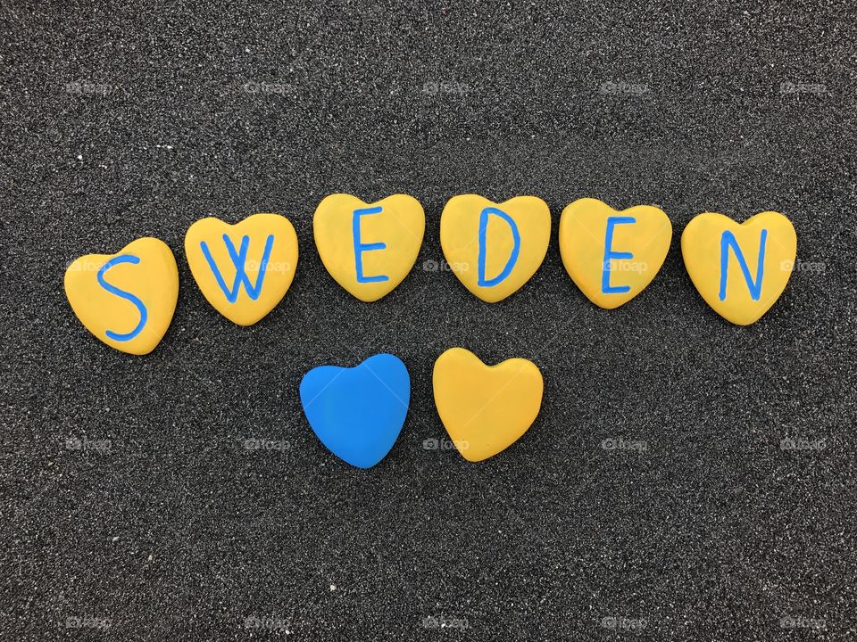 Sweden, country name on heart stones painted with national colors over black volcanic sand