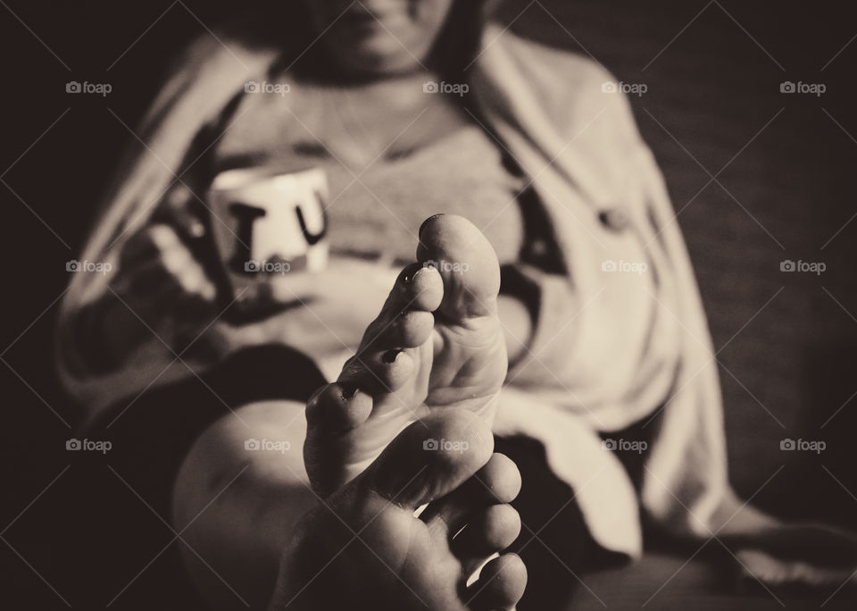 Black and white photo of woman relaxing, having a cup of coffee while resting her feet on the table