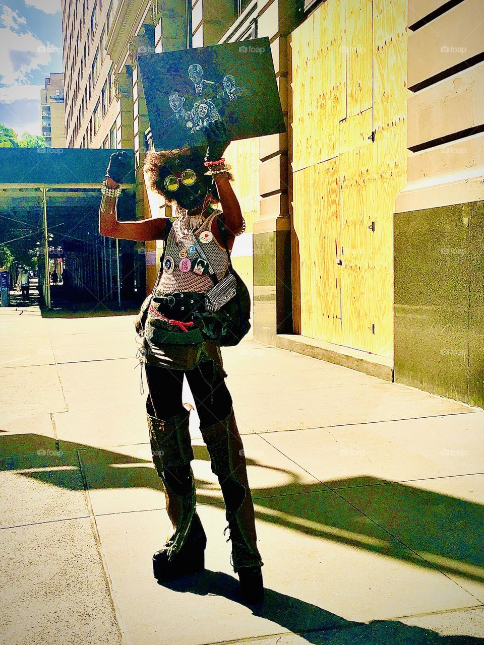 This streetartist with big 1970s style Afro hairdo, black face makeup, mirrored sunglasses and a hand drawn sign he/she is holding up was encountered on a bright sunny summertime afternoon in 2020 on 14th Street in Manhattan. Hypnotic Productions