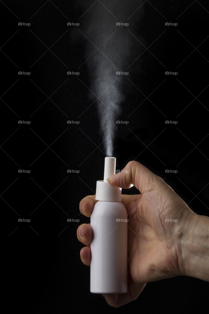 White container of spray bottle on black background. Hand holds medical  inhaler