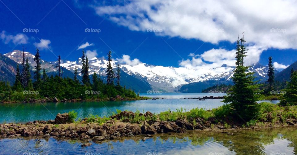 A gorgeous turquoise coloured glacial lake surrounded by tall peaks, rocky shores, alpine forests and a glacier.