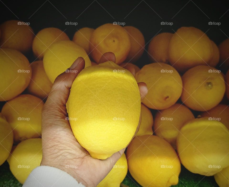 Lemon in a hand against lemons for background.