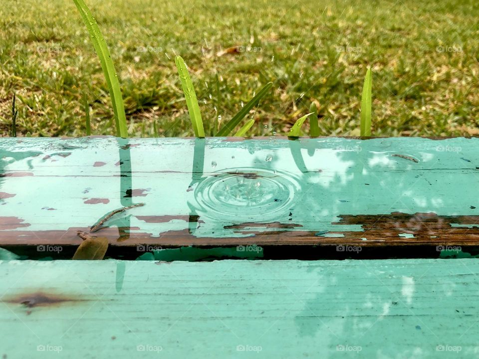 Raindrop splashing onto painted wooden porch step. The summer rain and sunlight on the weathered green step, the splash and the wet grass.