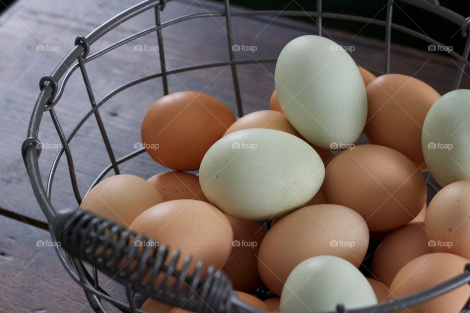 Farm-fresh blue and brown eggs in a wire basket on a dark wooden surface