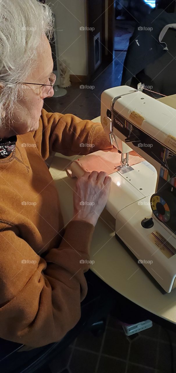 Stitcher, tailor, seamstress working at sewing machine working with fabric & threads.