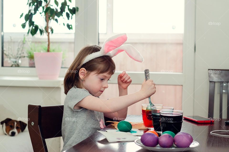 A little girl with Easter bunny ears decorates eggs.  Preparations for the celebration of Easter.