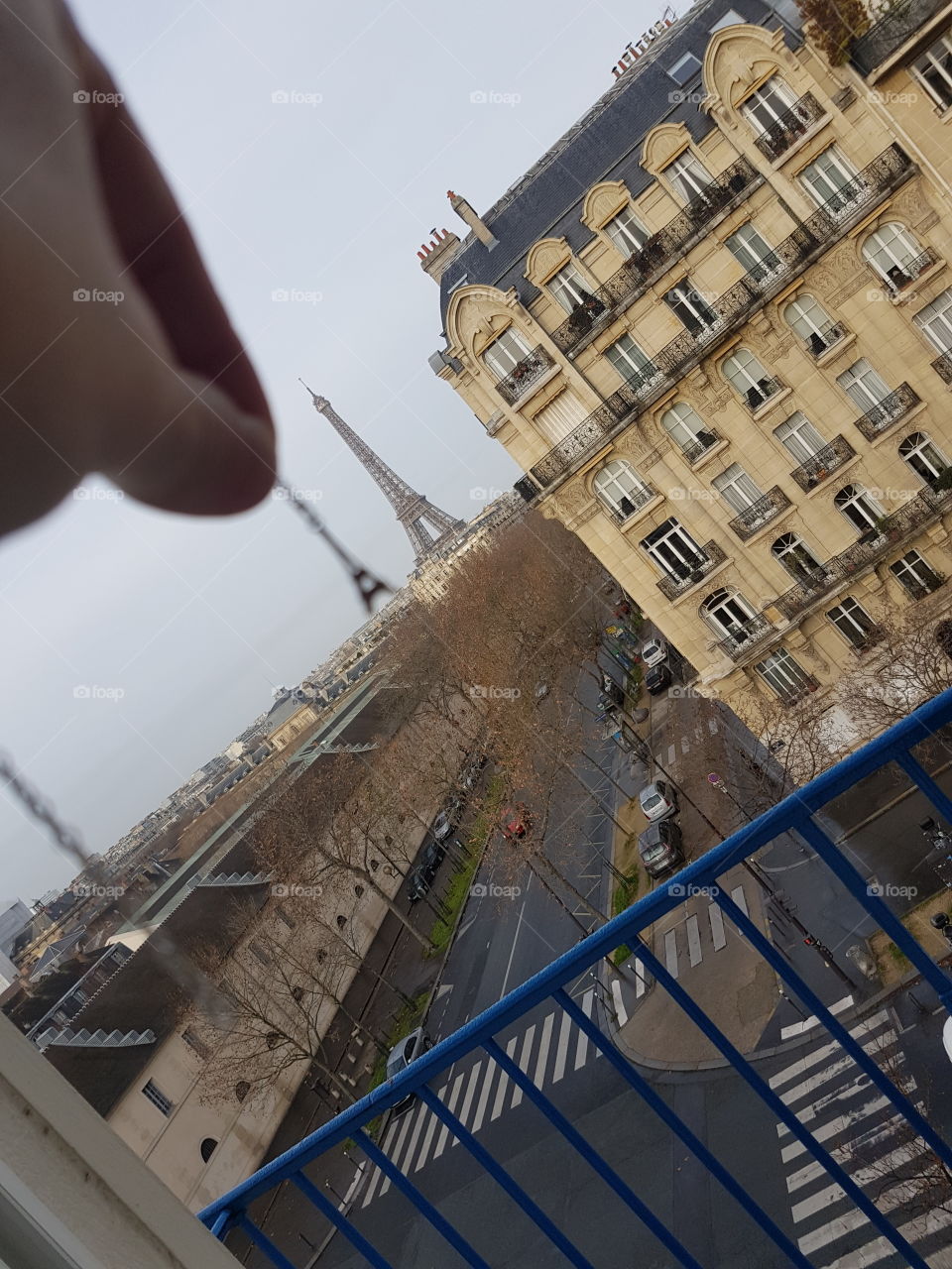 Hand holding a silver chain necklace with small charm of Eiffel tower from view of window balcony, same as real big Eiffel tower in Paris, France, Europe