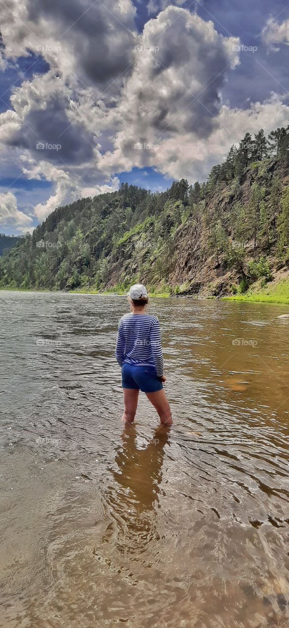 девушка в тельняшке стоит в воде на реке Мана и смотрит вдаль