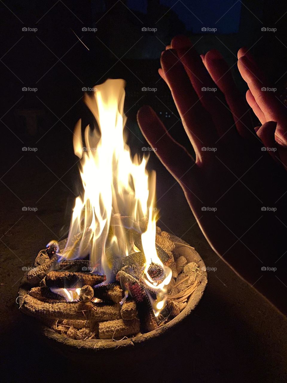 Some women are warming their hands next to a camp fire 