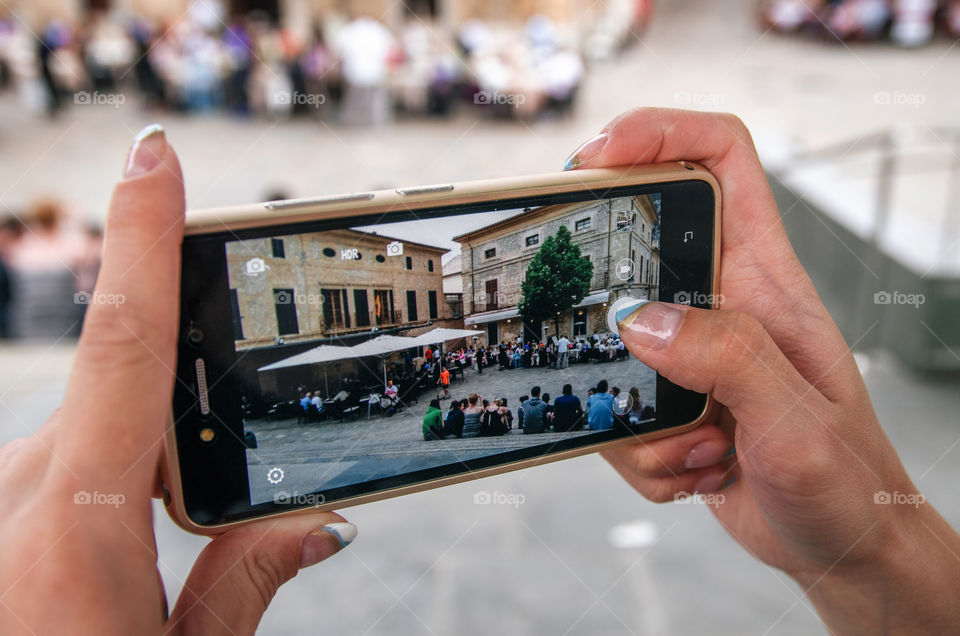 Young woman takes a photo of a crowded square in a medieval town, Mallorca, Spain. Hands with smartphone close up